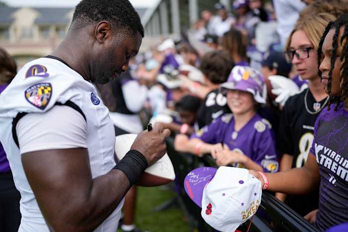 Roquan Smith autographs a small football as a crowd of kids stand behind the fence in front of him